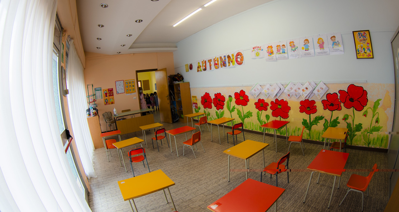 Aula luminosa con murales raffiguranti papaveri e i banchi colorati. Vista dal fondo dell'aula